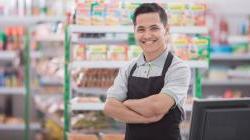 Young male shopkeep standing in convenience store smiling with arms crossed